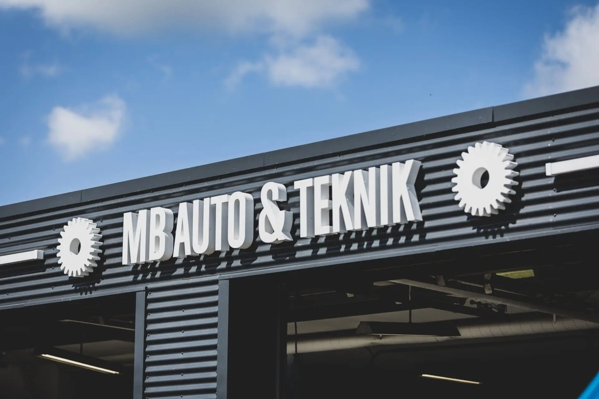 MB Auto & Teknik facade med hvide tandhjul mod blå himmel